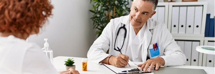 Actor portrayal of a healthcare professional seated at a desk speaking with another person in an office