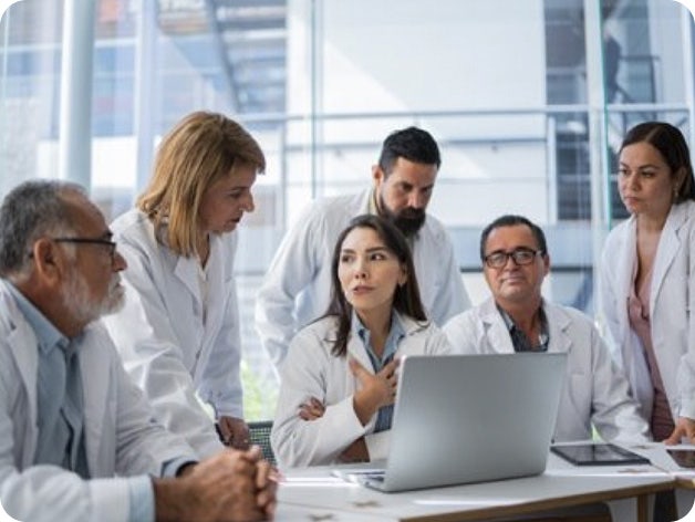Group of doctors in white lab coats gathered around a laptop