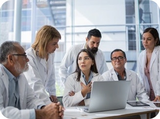 Group of doctors in white lab coats gathered around a laptop