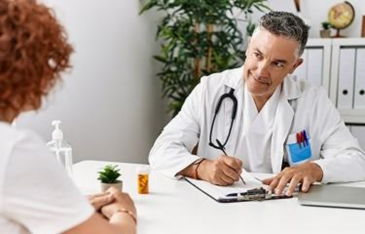 Actor portrayal of a healthcare professional seated at a desk speaking with another person in an office
